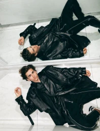 Young man in a black leather jacket lying on a reflective tiled floor styled by James Yardley