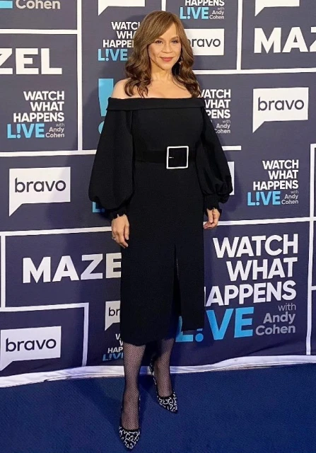 Rosie Perez poses in a black off-the-shoulder midi dress with a square belt buckle at 'Watch What Happens Live' with Andy Cohen.