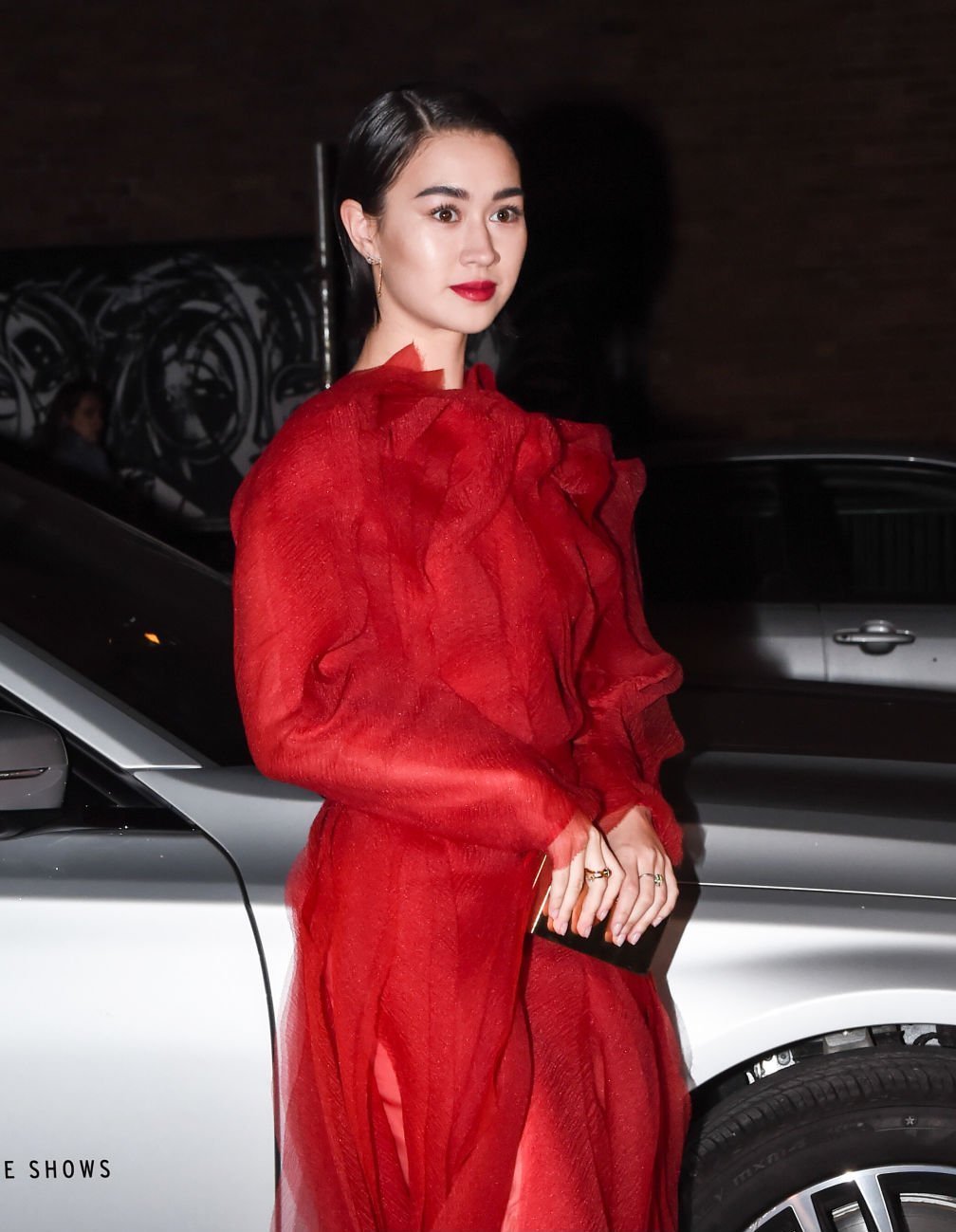 Woman in a sheer red dress posing next to a silver car in New York styled by Jared Depriest