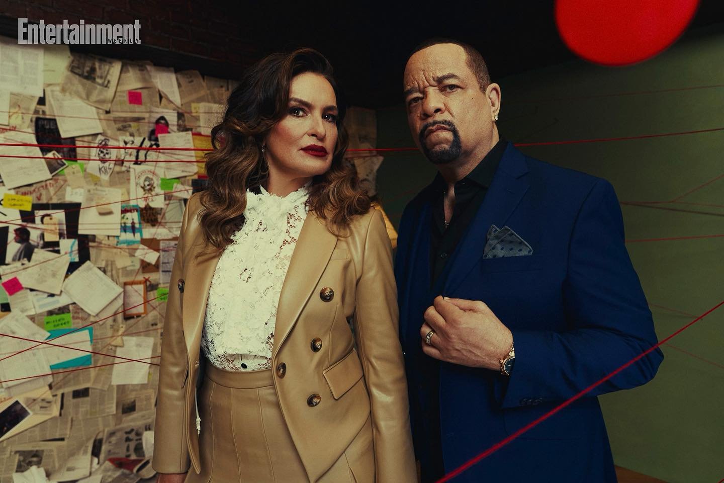 Portrait of Ice-T and Coco Austin posing in a studio with a crime board in the background; they are wearing formal wear and serious expressions.