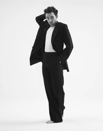 Man wearing a black suit jacket and trousers with a white t-shirt against a plain white background