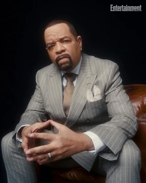 Portrait of Ice-T in a grey pinstripe suit and tie, seated in a brown leather chair against a dark backdrop, with Entertainment logo visible.