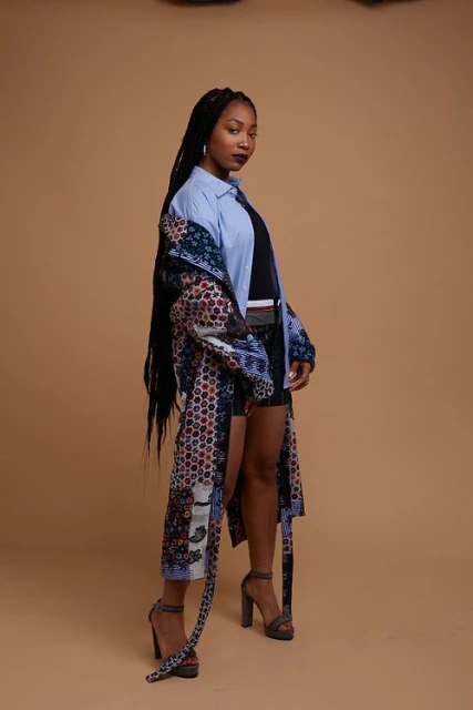 A woman with long braids, wearing a floral duster, poses in a studio with a neutral background, showcasing fashion and style.