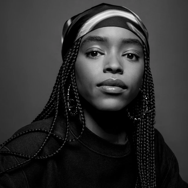 Black and white portrait of a young African-American woman with braided hair and a patterned headscarf, wearing hoop earrings.