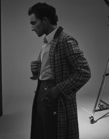 Monochrome portrait of a man in profile wearing a plaid coat and white button-down shirt in a studio setting.