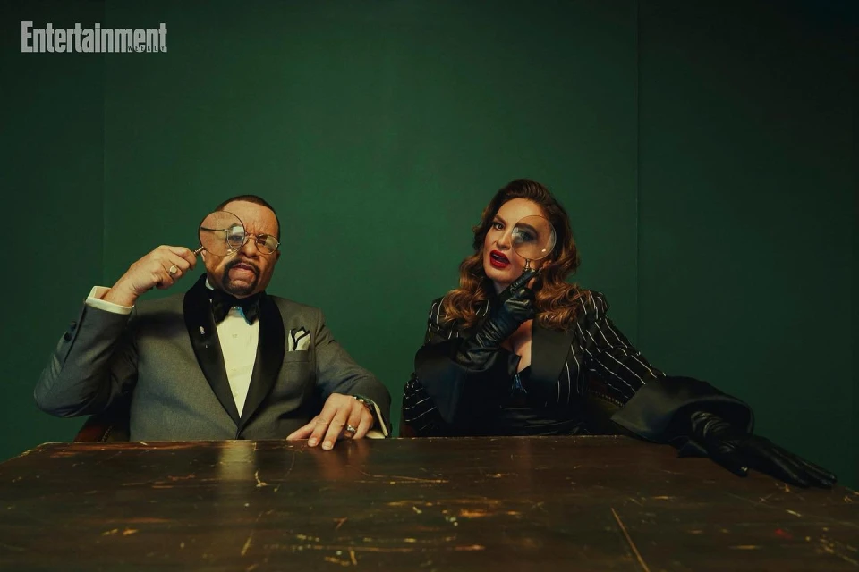 Elegant shot of a man and woman in formal attire seated at a table, holding magnifying glasses with a green backdrop.