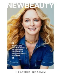 Heather Graham wearing a denim top with a gold chain necklace against a light grey background