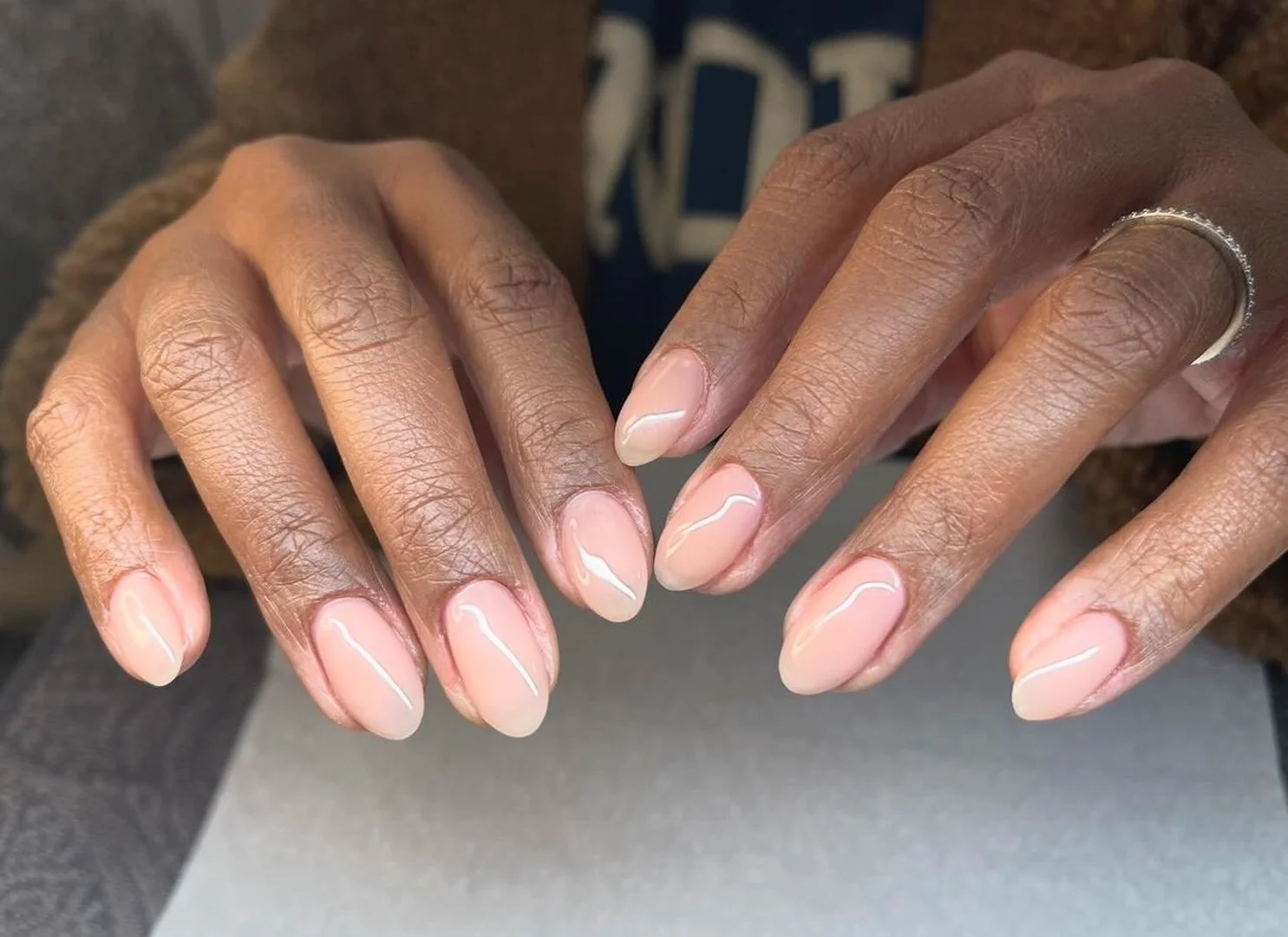 Close-up of hands with neutral nail polish on an adult female.  Hands are well manicured, and a silver ring is visible on one finger.
