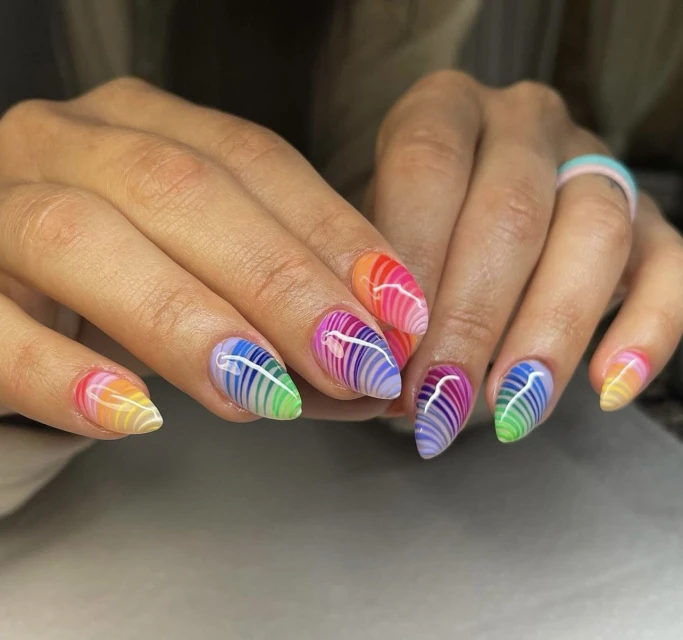Close-up of a woman's hands showcasing rainbow-striped nail art, emphasizing the colorful and detailed manicure design.