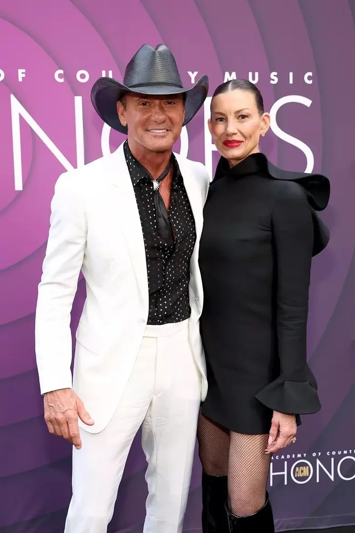 Country music stars Tim McGraw and Faith Hill pose on the red carpet at an awards event, wearing formal attire and elegant jewelry.