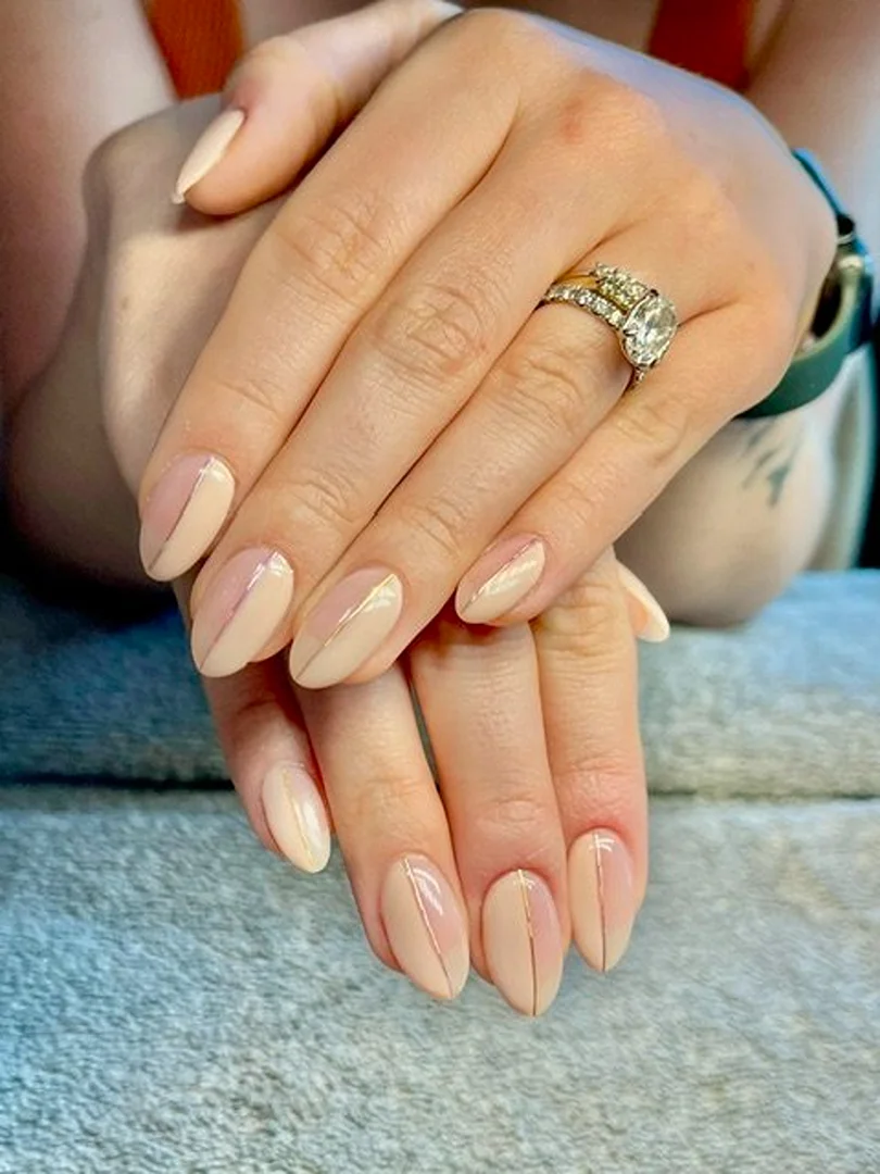 Close-up of a woman's hands showcasing a geometric-design manicure with nude and light-pink nail polish and wearing an engagement ring.