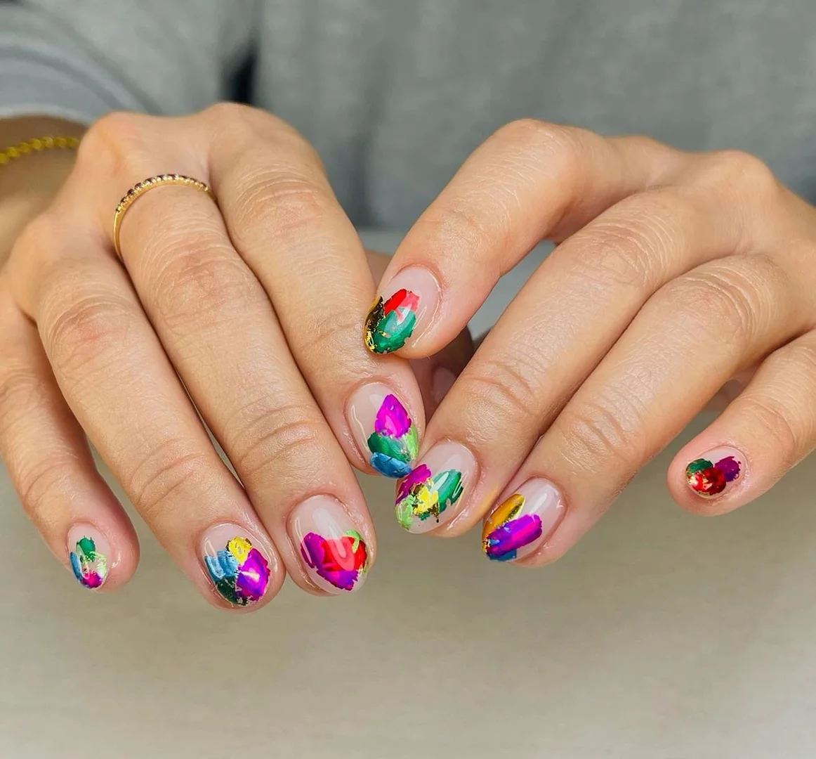 Close-up of a woman's hands featuring a colorful abstract painting design on her fingernails. The nails are short and natural.