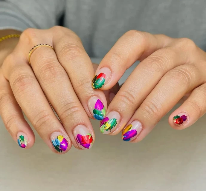 Close-up of a woman's hands featuring a colorful abstract painting design on her fingernails. The nails are short and natural.