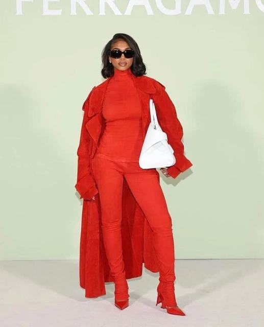 Woman poses in red outfit with sunglasses and white purse against a pale green backdrop with the Ferragamo logo visible.