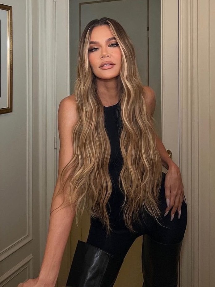 Khloe Kardashian with long highlighted hair wearing a black outfit posing indoors