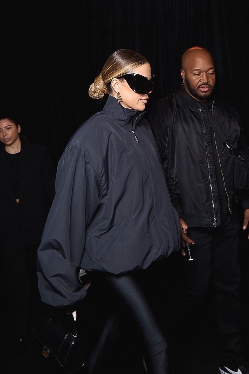 Khloe Kardashian wearing oversized black jacket and sunglasses with security guard in background