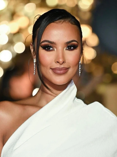 Portrait of a glamorous adult woman with a neutral facial expression wearing a white dress and long earrings against a blurred background.