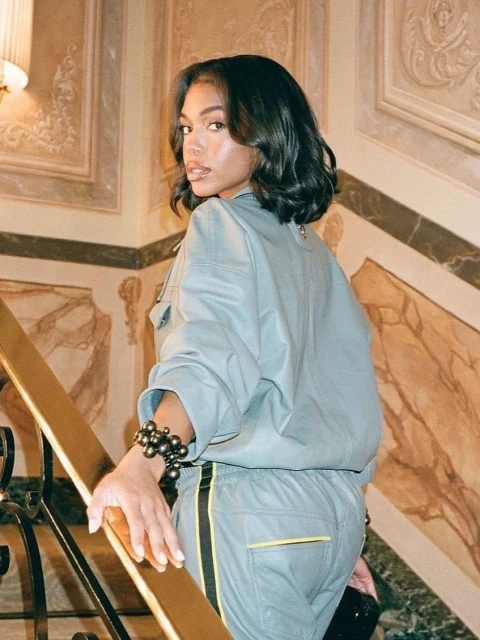 Woman on stairs looking over shoulder wearing matching grey top and pants with black stripe, black bead bracelet, and holding a purse.