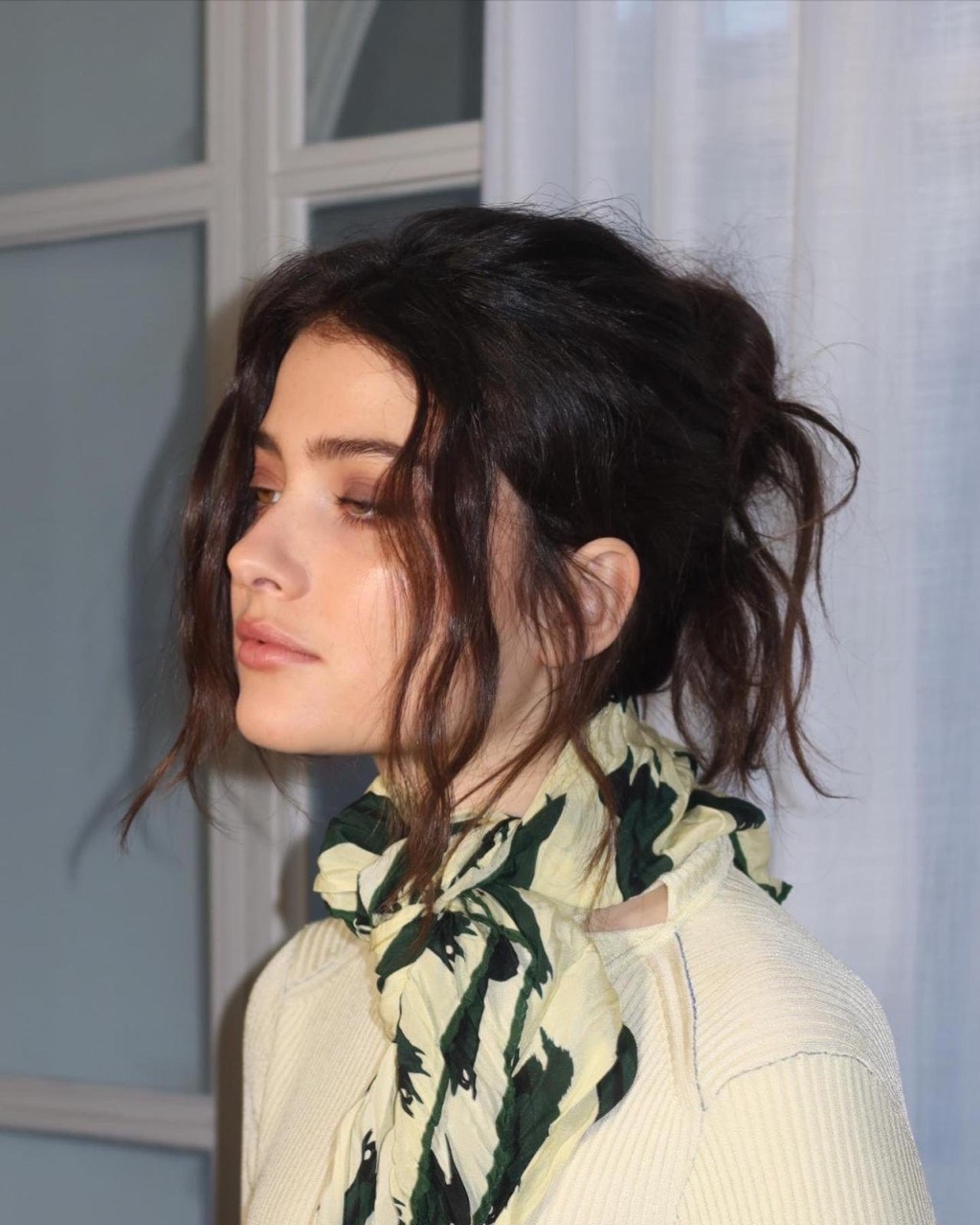 Close-up portrait of a brunette woman with a patterned scarf, set against a neutral interior. The soft lighting accentuates the subject.