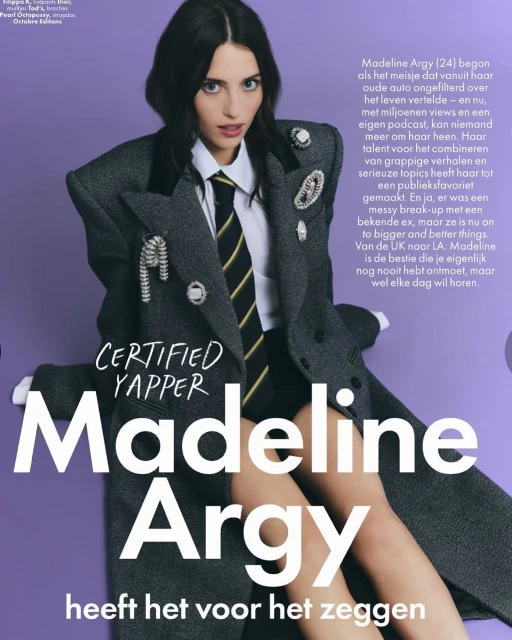 Portrait of Madeline Argy in oversized grey suit jacket, white shirt, and striped tie against a light purple backdrop, posing for a magazine.