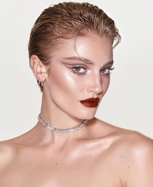 Close-up beauty shot of an adult female with wet-look hair, dark lipstick, and a sparkling diamond necklace, against a plain white backdrop.