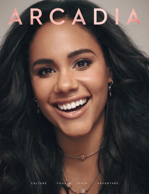 Close-up studio shot of a smiling woman with dark hair wearing a necklace and earrings, overlaid with the pink-lettered 'Arcadia' magazine title.