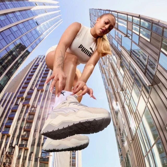Eye-level wide shot of a woman posing in sportswear with modern skyscrapers, showcasing athletic wear and urban fashion against a blue sky.