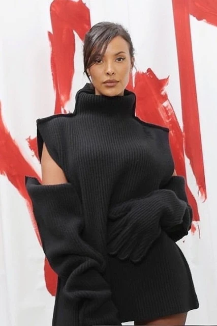 Portrait of a woman wearing a black, high-neck knit dress with detached sleeves and gloves against a white and red background.