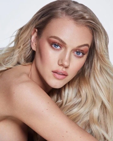 Close-up portrait of a woman with long blonde hair, blue eyes, and soft makeup against a neutral backdrop.