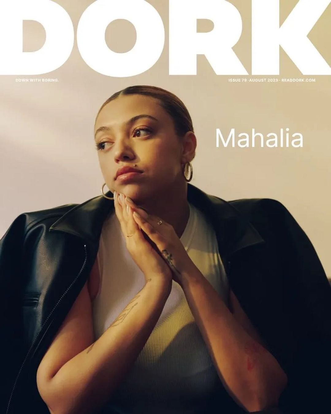 Close-up of a young woman with light skin and dark hair in a black leather jacket for a magazine cover, indoors with soft lighting.