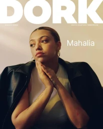 Portrait of Mahalia wearing a white top and black leather jacket with gold hoop earrings against a neutral background.