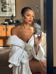 Woman taking a mirror selfie wearing a white plush bathrobe with styled dark hair and bold red lipstick