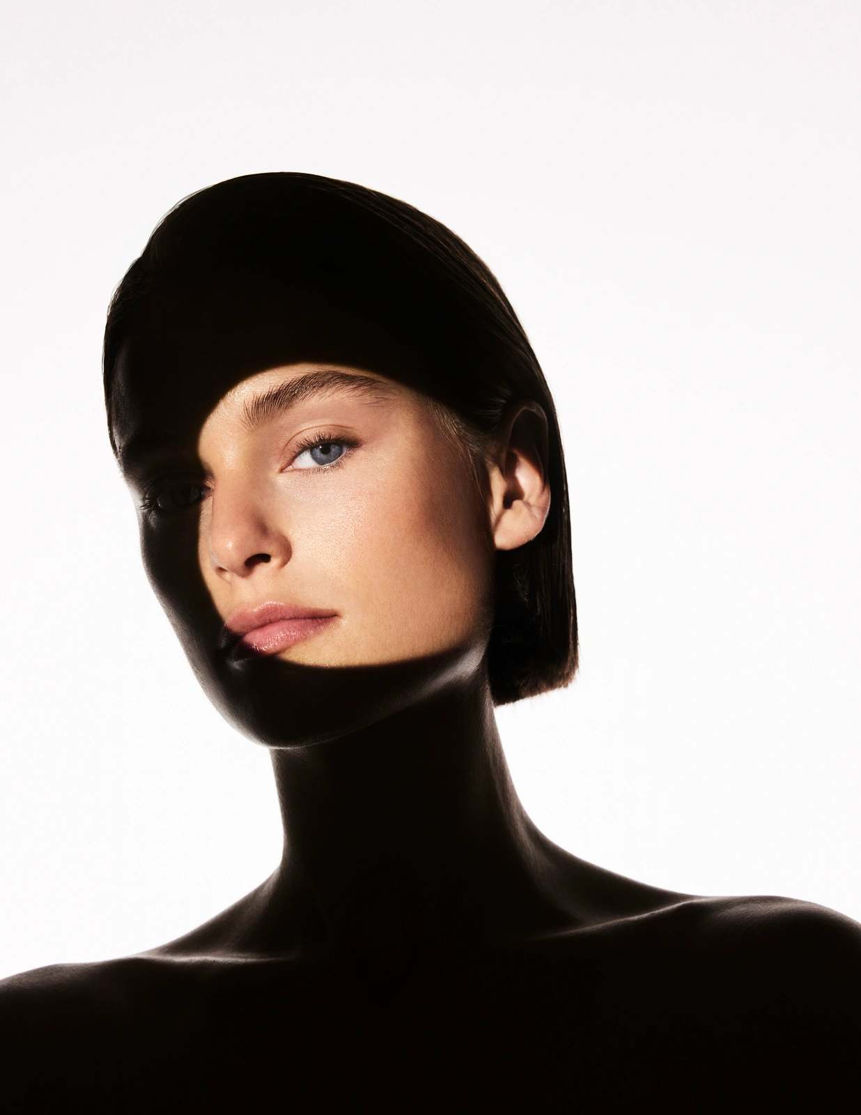 Close-up beauty portrait of a woman with dramatic graphic black shadow framing her face against a bright white background.