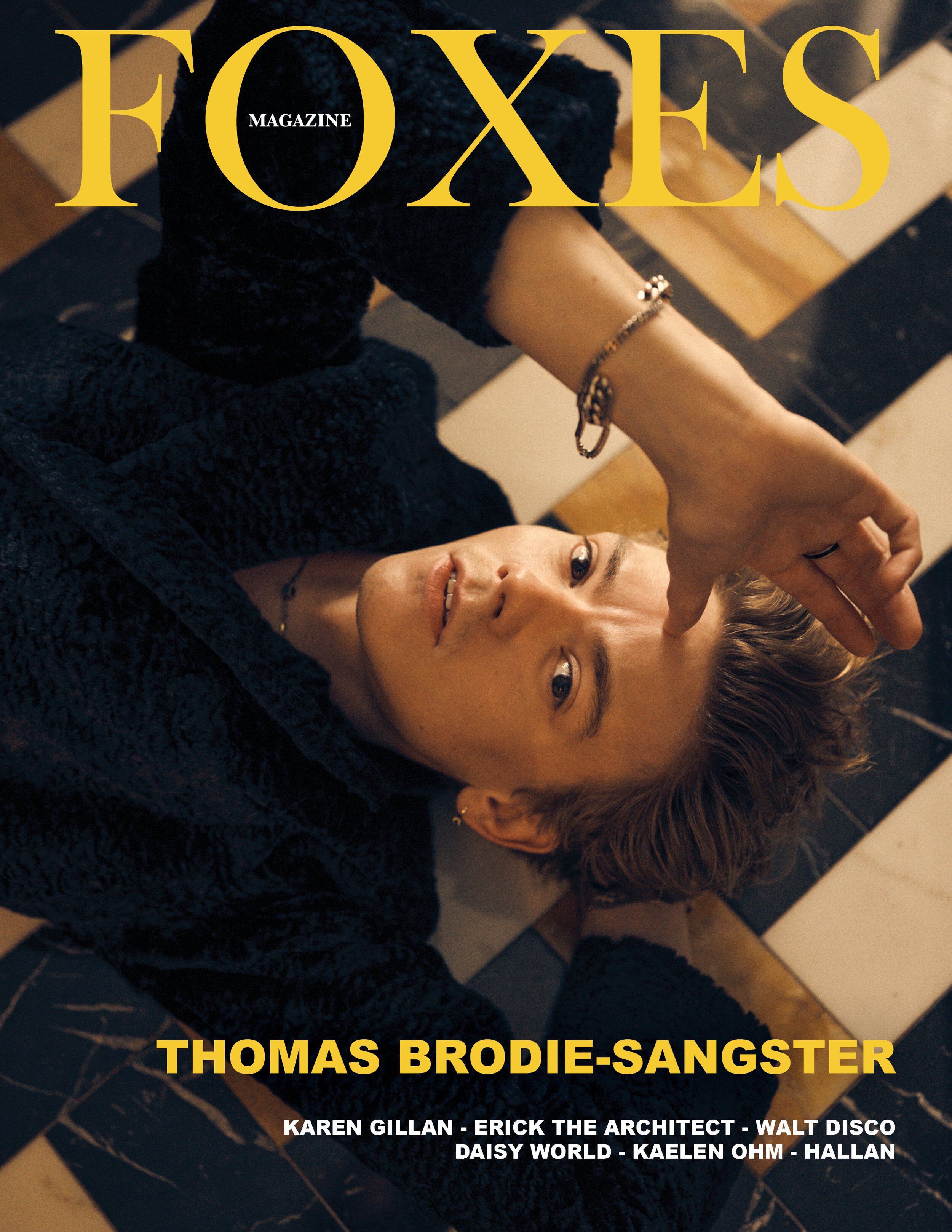 Magazine cover shot of Thomas Brodie-Sangster laying on a herringbone marble floor wearing a dark sweater and silver bracelet, Foxes Magazine.
