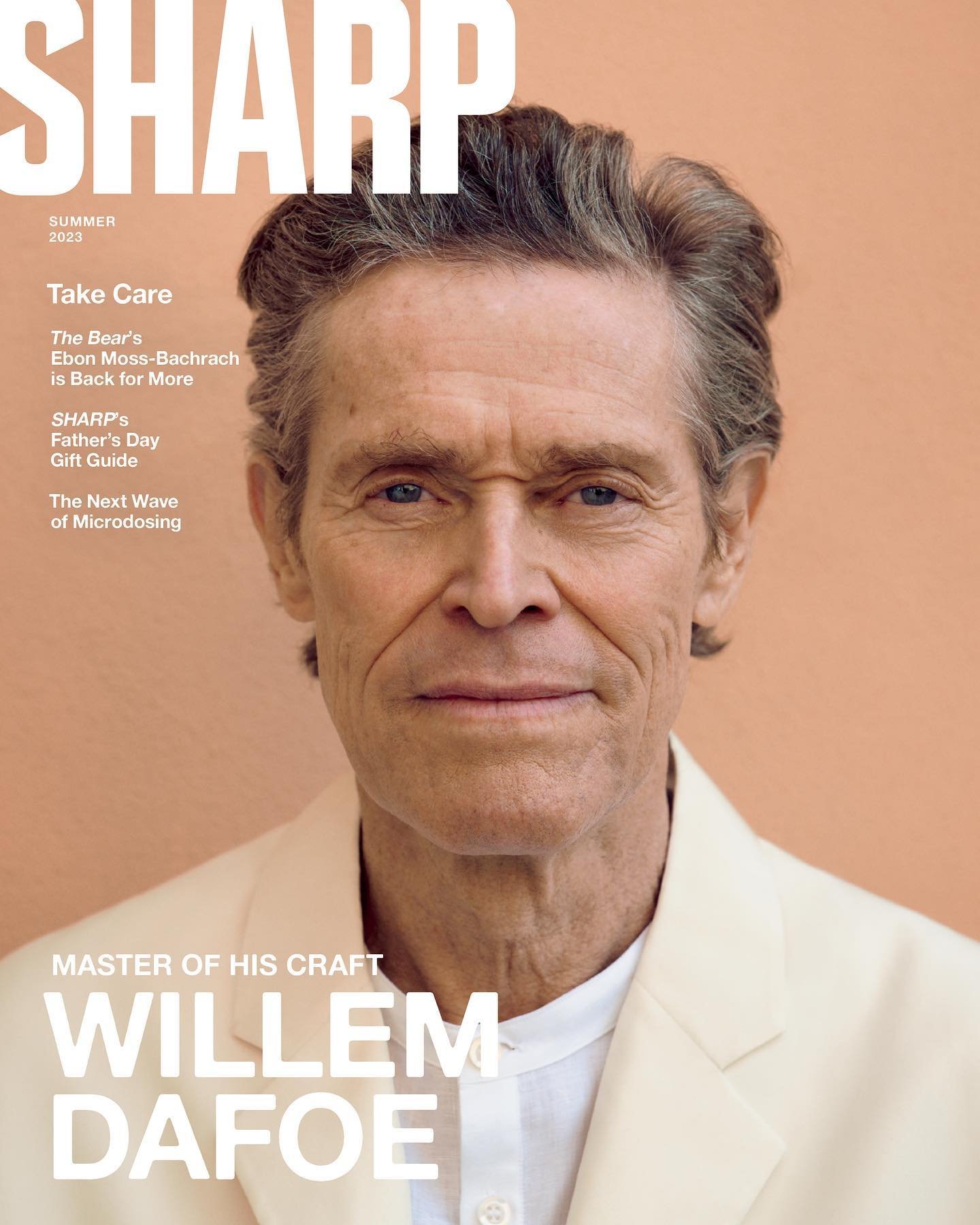 Willem Dafoe on the cover of Sharp Magazine Summer 2023 edition; portrait of the actor wearing a light-colored jacket on a peach background.