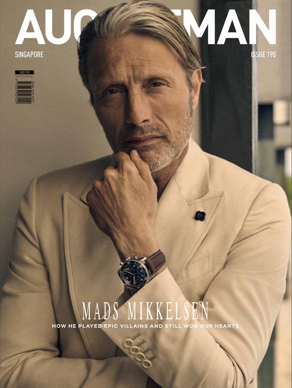 Magazine cover featuring Mads Mikkelsen in a light-colored suit, looking thoughtfully at the camera, with architecture background.
