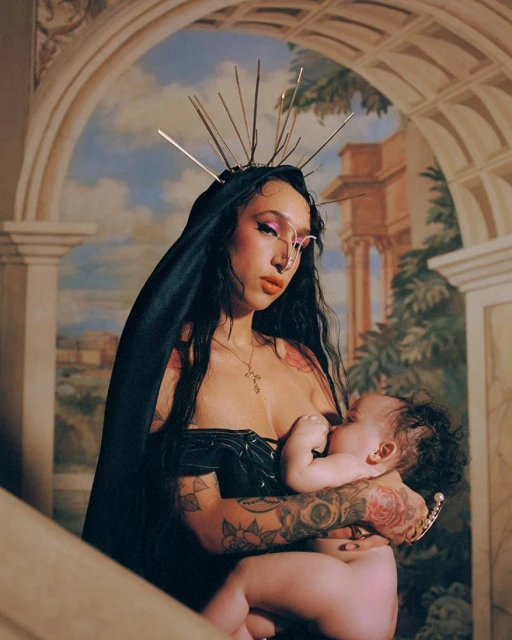 Woman with spiked crown and tattoos breastfeeding a baby against an arched, classically-styled background in an indoor setting.