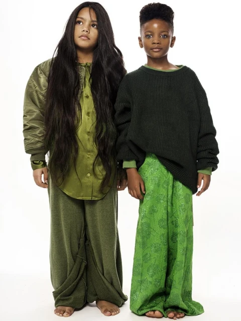 Two children pose in olive green and lime green outfits against a bright white backdrop in a fashion studio shot. 