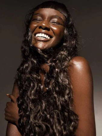 Close-up portrait of a smiling African-American woman with curly dark hair, shiny skin, and a toothy smile against a dark background.