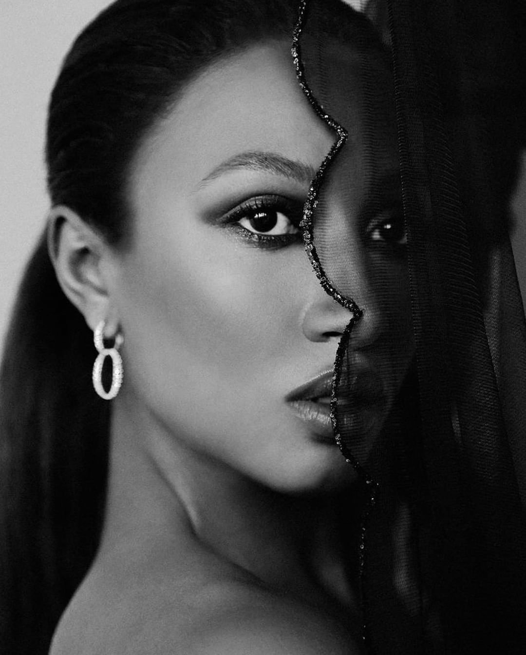 Close-up portrait of a woman in black and white wearing a sheer dark veil and hoop earrings