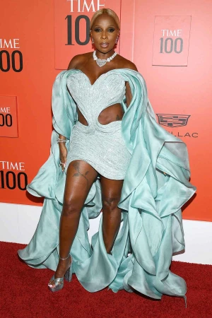 Mary J. Blige poses on a red carpet in a light-blue dress with pearl jewelry for the Time 100 event, smiling at the camera.