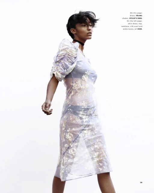 Fashion editorial shot of a Black female model wearing a floral print dress, posing against a bright white background in a studio setting.