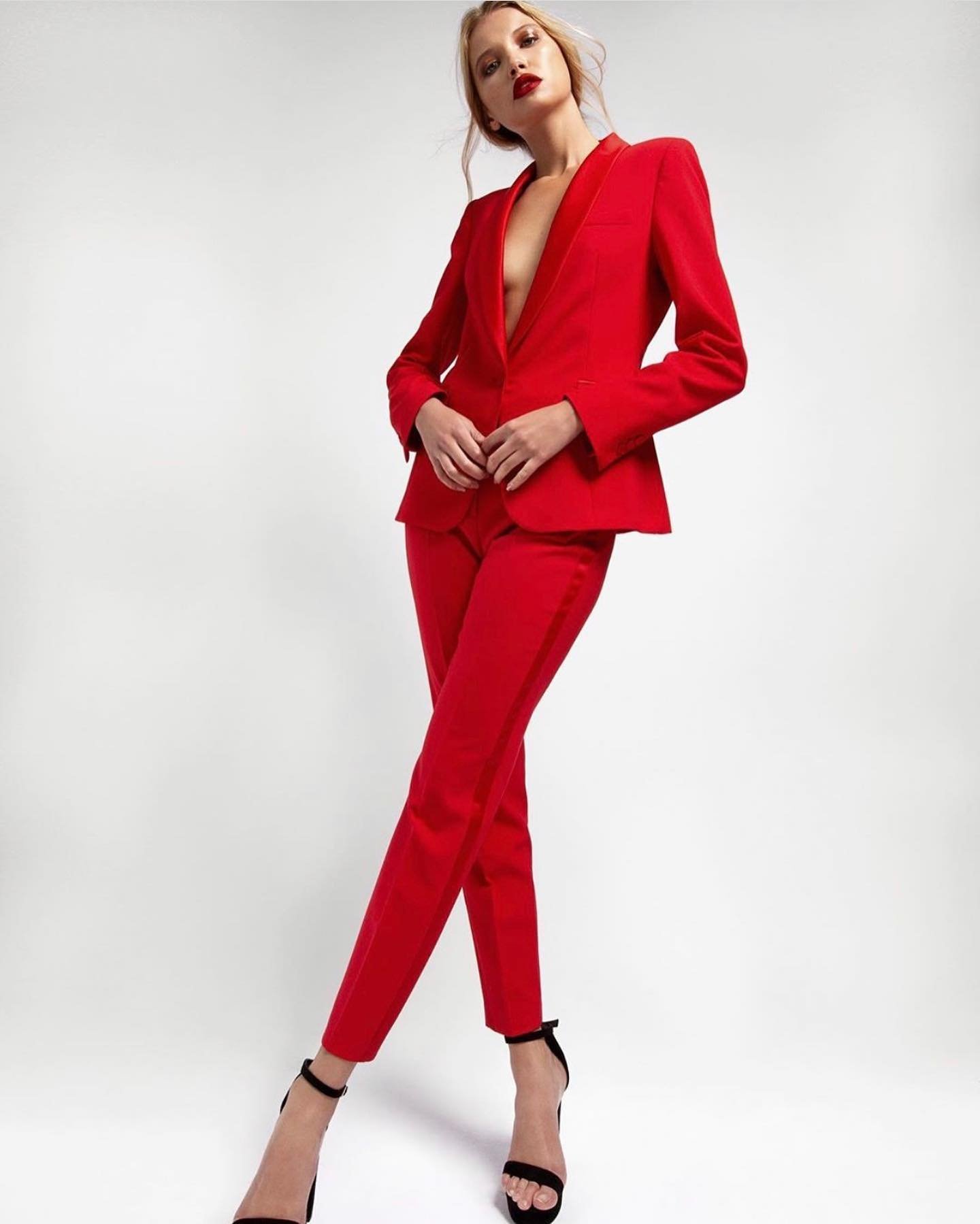 Woman poses in a red pantsuit and black high heels against a white backdrop, creating a bold and stylish visual composition.