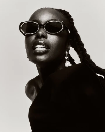 Black woman wearing jeweled sunglasses and braided hair styled by Jazmin Kelly against a neutral background