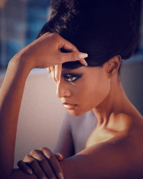 Close-up portrait of a woman with dramatic dark beehive updo hairstyle resting her hand gently on her forehead