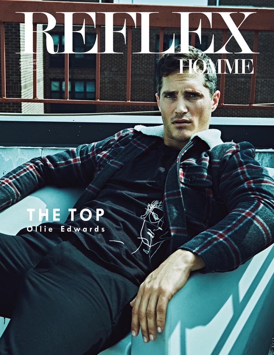 Male model in a plaid jacket lounges in a chair on a rooftop with a city view; Reflex Homme magazine cover; fashion photography.