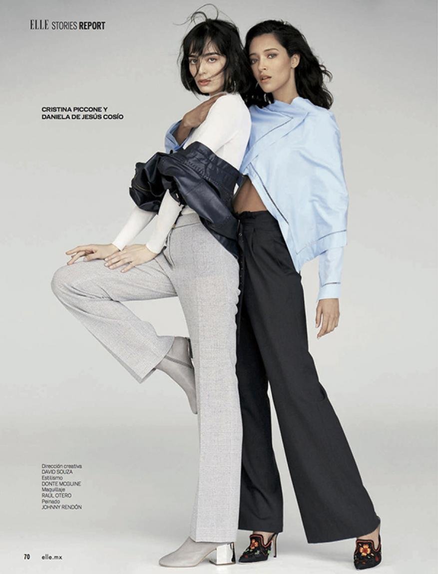 Two fashion models pose indoors with stylish trousers and tops in a studio setting. One model wears gray, the other wears black trousers.
