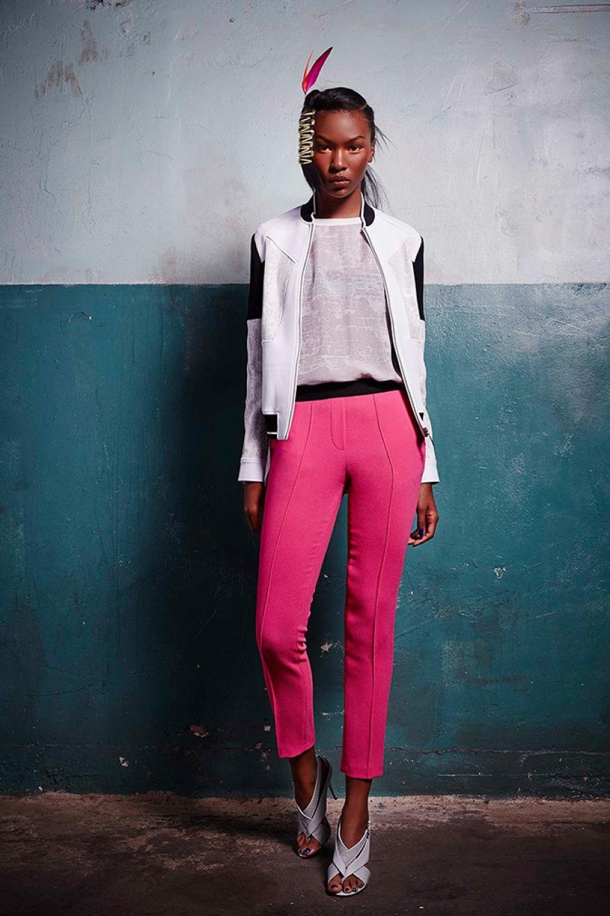 Full-length portrait of an African-American fashion model in a white jacket and hot pink pants, posing indoors against a blue wall.
