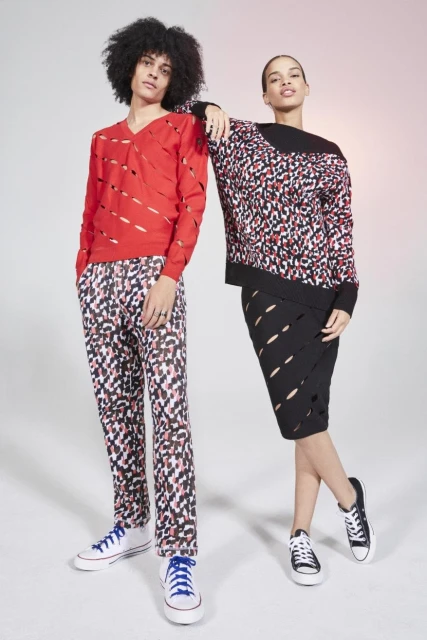Two models pose in a studio wearing knitwear. The male model is wearing a red sweater and patterned pants, while the female model wears a sweater and skirt.