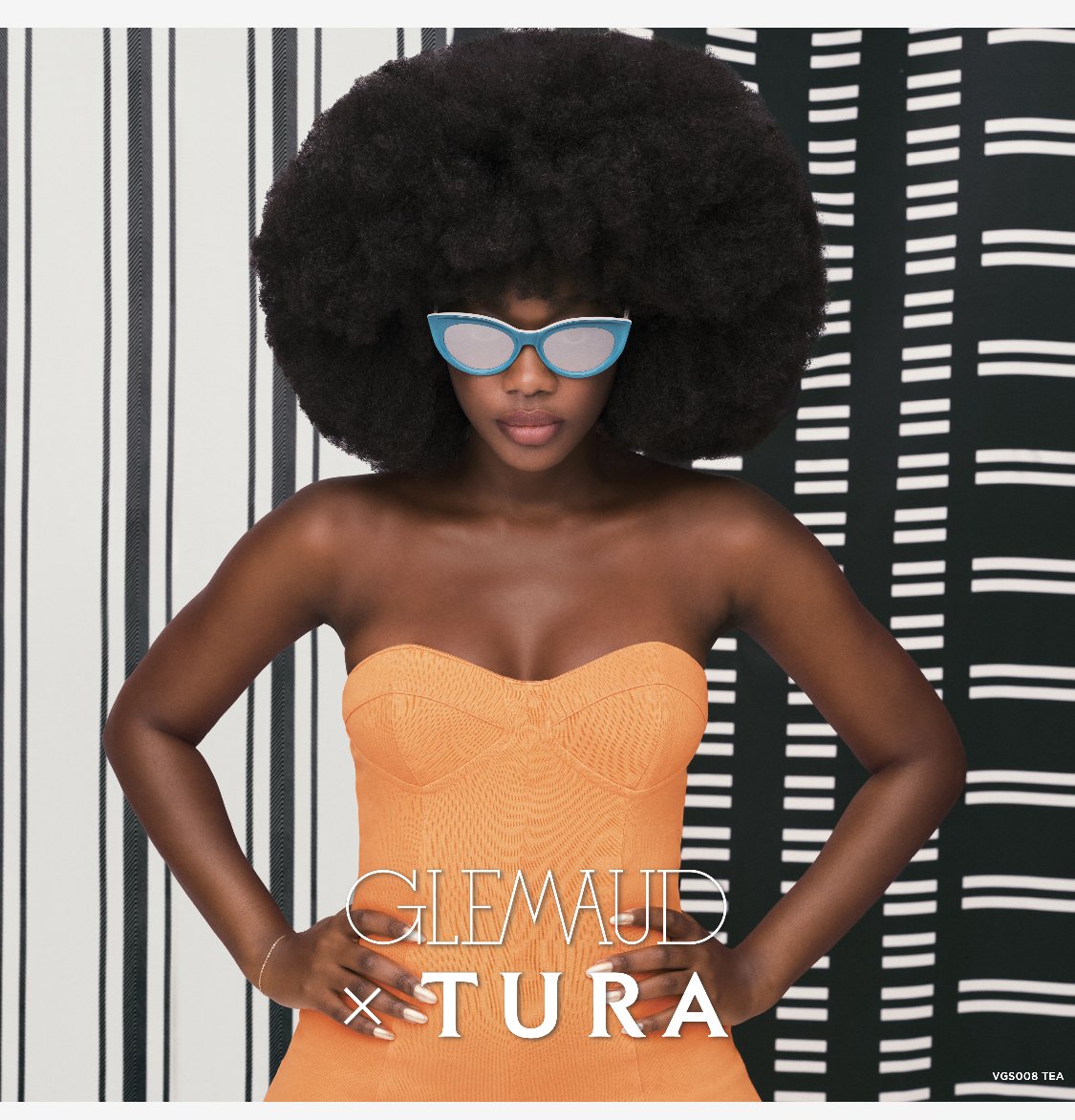 Glamorous young woman with large afro hairstyle poses in an orange dress and stylish sunglasses in front of a striped backdrop.